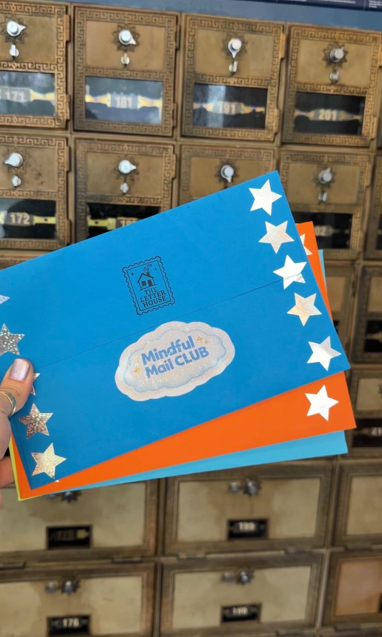A blue Mindful Mail Club envelope at a wall of post office boxes